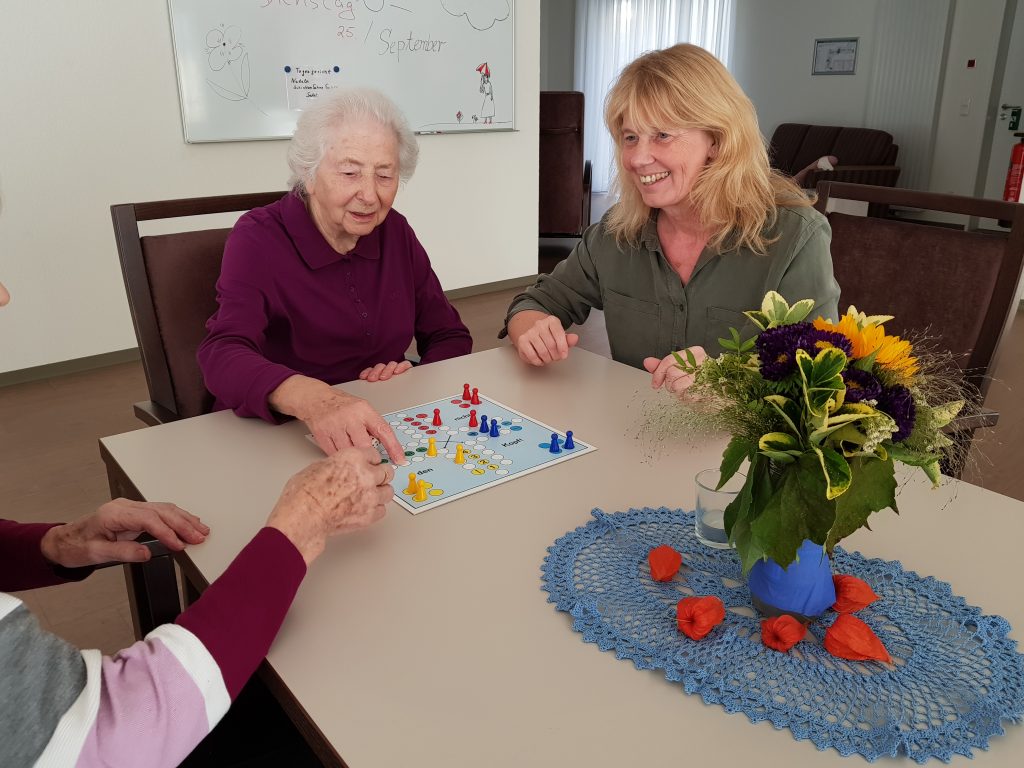Gemeinsam mit der 92-jährigen Bewohnerin Katharina Kiwitt und einer weiteren Bewohnerin spielt Walburga Volkhausen eine Runde Mensch ärger dich nicht. Foto: ST. JOHANNISSTIFT