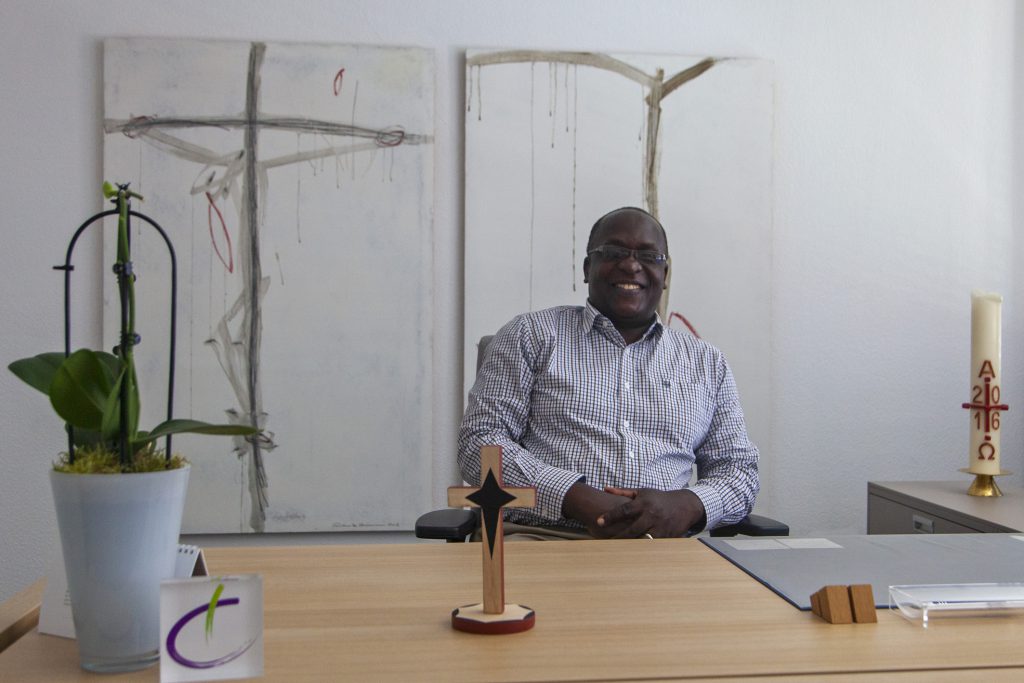 Gut gelaunt: Superintendent Frederick Muganyizi am Schreibtisch seines Kollegen Volker Neuhoff. Das Holzkreuz aus Tansania hat schon seinen Platz gefunden. Foto: Wolfgang Dzieran