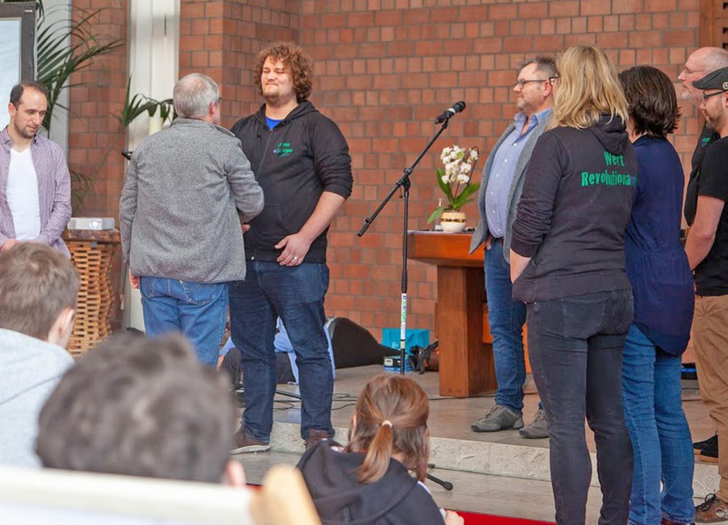 Pfarrer Thomas Fischer (von hinten) gratuliert hier Jugendreferent Jonas Mischendahl zu seiner Einführung. Das Bild zeigt weitere Pfarrerinnen und Pfarrer sowie Hauptamtliche des Jugendreferats.