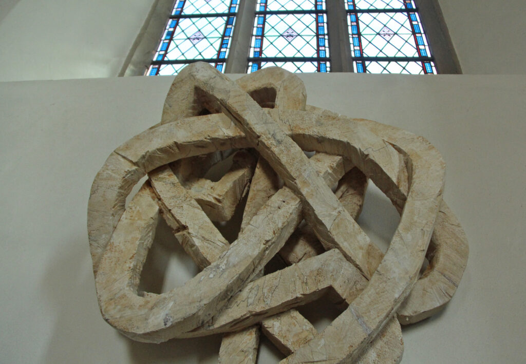 Eine Holzplastik wie ein Knotengewühl unter einem Fenster im Nordschiff der Kirche. Foto: Burkhard Battran