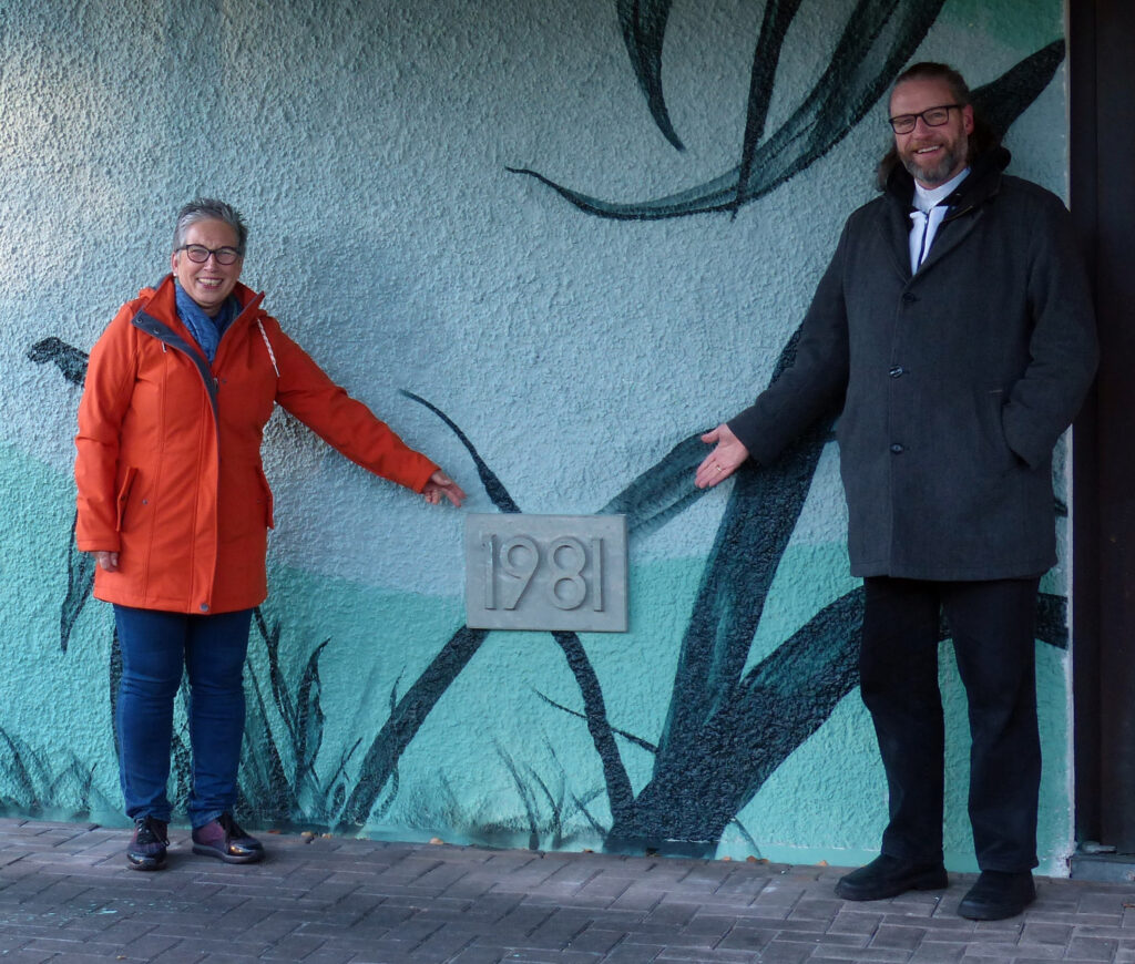 Der Grundstein verweist auf das Gründungsjahr – Evelyne Schubert (Vorsitzende des Presbyteriums, li.) und Pfarrer Oliver Peters (re.) freuen sich über den runden Geburtstag der Paul-Gerhardt-Kirche Foto: Ev. Kirchengemeinde Schloß Neuhaus