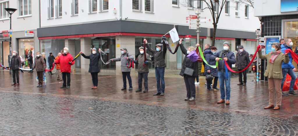 Die Teilnehmenden aus evangelischen Kirchengemeinden und dem Kirchenkreis Paderborn, darunter Superintendent Volker Neuhoff mit der Fahne des Kirchenkreises, freuen sich darüber, dass die Menschenkette zwischen Rathaus und St. Vincenz-Krankenhaus geschlossen werden konnte. Foto: EKP/Oliver Claes