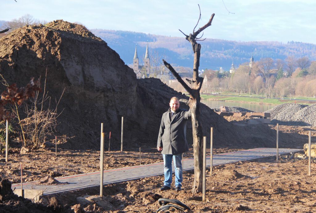 Pfarrer Tim Wendorff an einem verkohlten Baum, der im Schöpfungsgarten die Kraft des Feuers symbolisiert. Der Erdhaufen, der die Sicht auf die Weser versperrt, wird noch zur Geländemodulation benötigt und später verschwunden sein.Foto: Burkhard Battran 