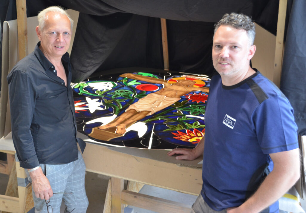 Prokurist Christoph Sander (v. l.) und Glasmaler Eduard Schizle, Glasmalerei Peters, präsentieren die bemalten und gebrannten Gläser.Foto: Abdinghof-Bezirk 