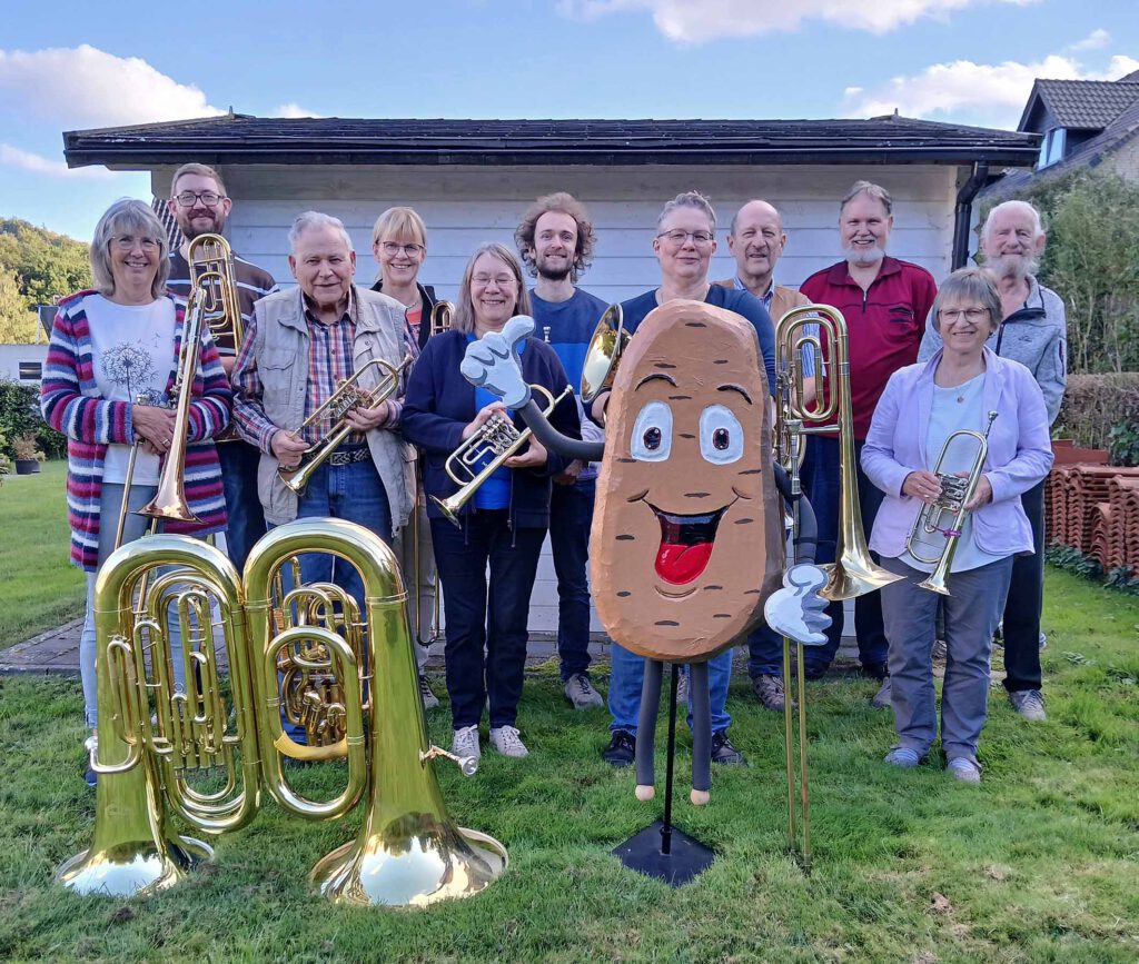 Blechbläser und Blechbläserinnen mit ihren Instrumenten und einem Aufsteller mit einer Figur in Form einer Kartoffel.