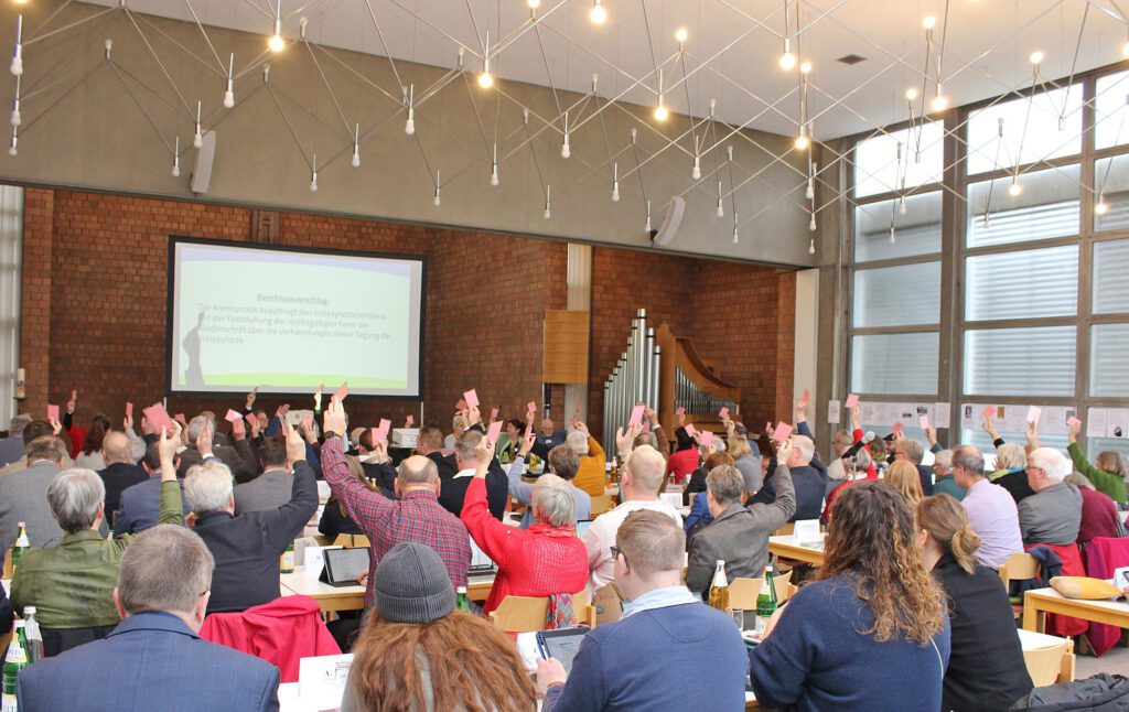 Die Abgeordneten der Kreissynode im Paderborner Martin-Luther-Zentrum heben bei einer Abstimmung ihre Stimmkarten.