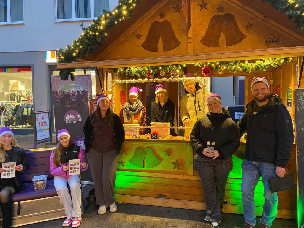 Junge Menschen in und vor einer Hütte auf dem Weihnachtsmarkt in Paderborn.