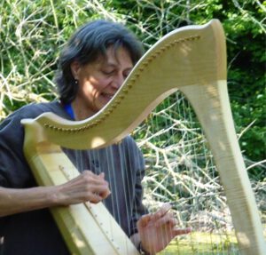 eine Frau die eine Harfe spielt und im Grünen sitzt