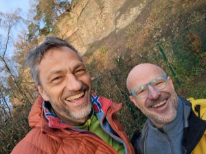 zwei lachende Männer im Hintergrund Steine und Bäume
