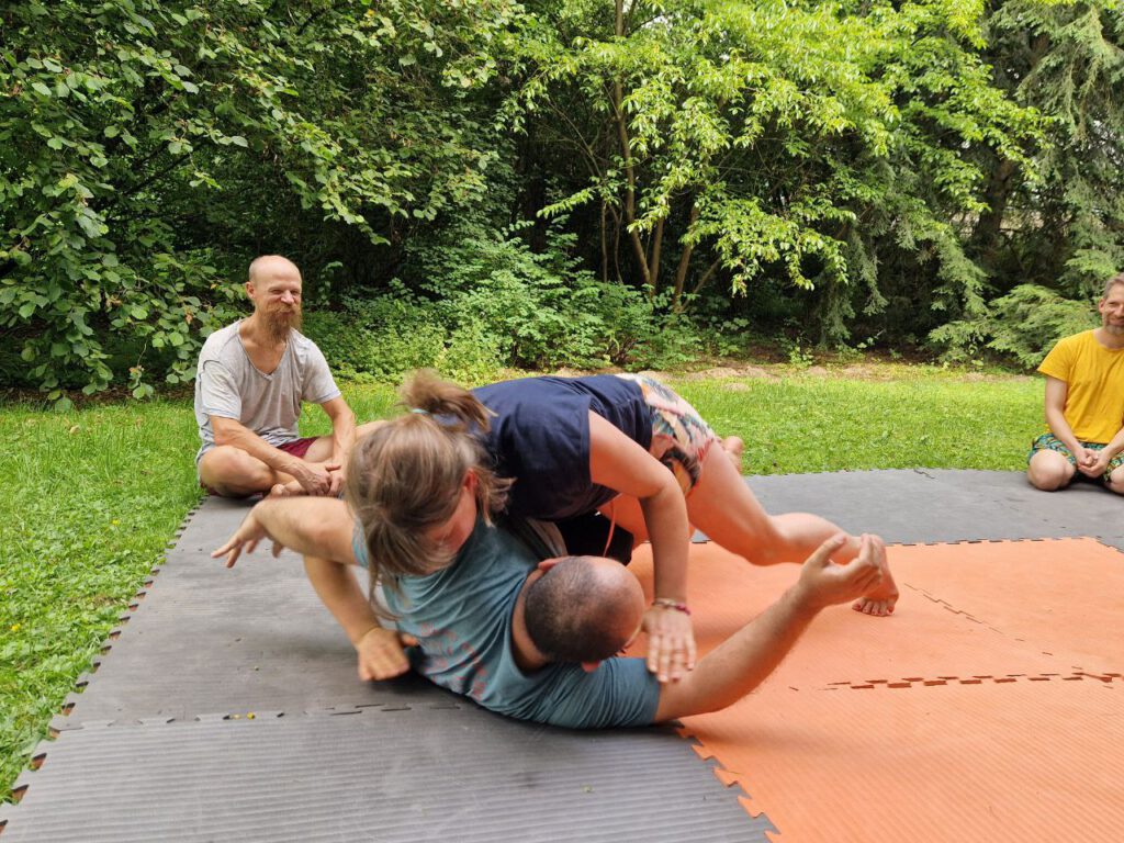 zwei Personen raufen sich spielerisch auf der Matte, andere Personen gucken zu