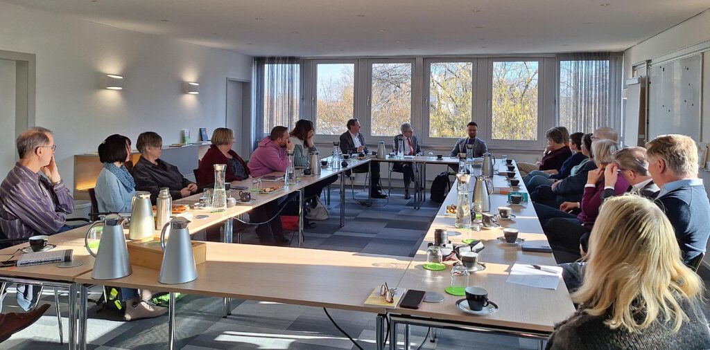 Die Teilnehmenden sitzen an Tischen in einem Konferenzraum.