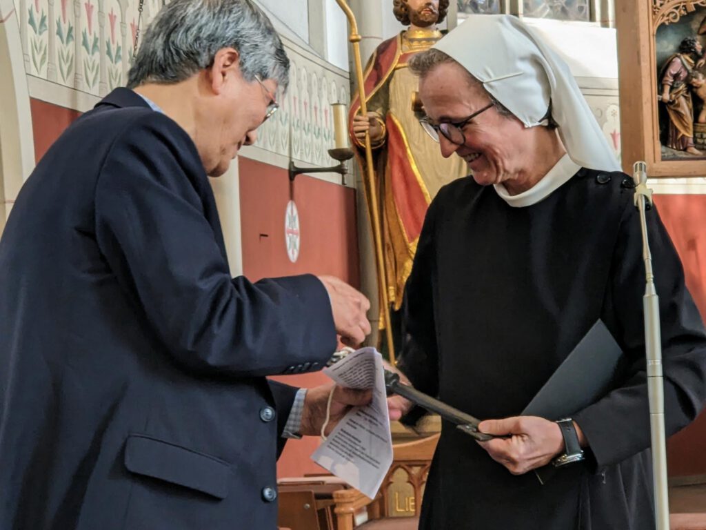 Zwei Personen übergeben symbolische Schlüssel in einer Kirche.