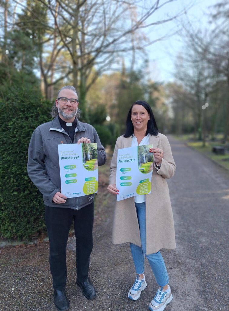 Zwei Personen halten Plakate für das Friedhofscafé in den Händen.
