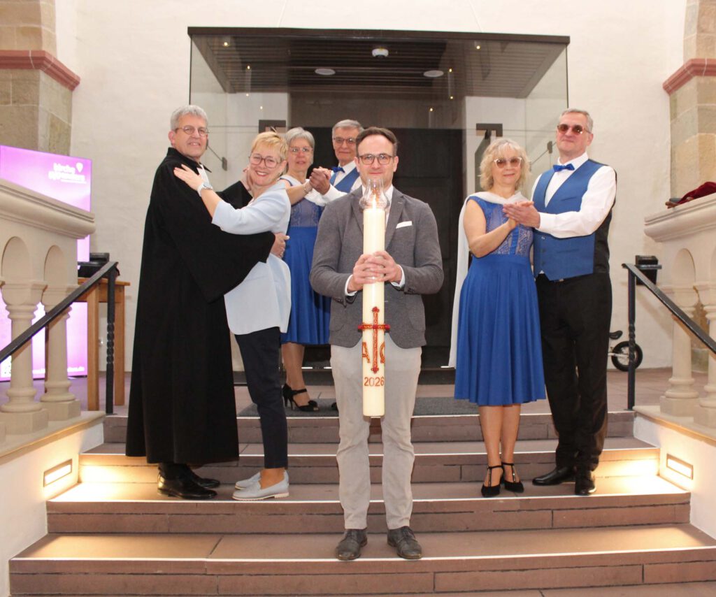 Menschen stehen in Tanzhaltung auf den Stufen in der Kirche, eine Person trägt eine Osterkerze