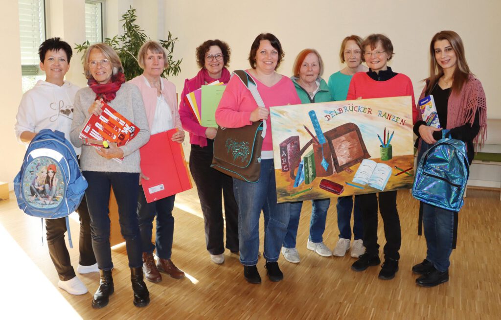 Menschen, die beim Delbrücker Ranzen mitarbeiten, halten Schulmaterialien und ein Transparent in den Händen.