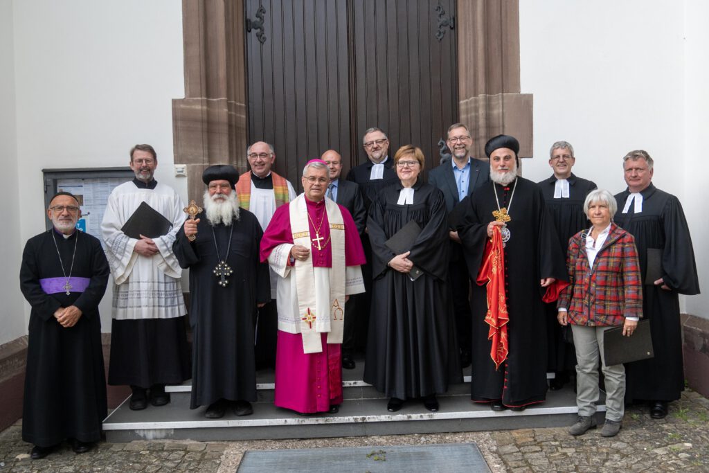 Menschen als Vertreter verschiedener Konfessionen stehen als Gruppe vor einer Kirchentür.