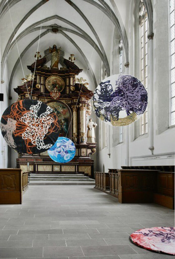 Farbige Kunstobjekte schweben in einer historischen Kirche. 