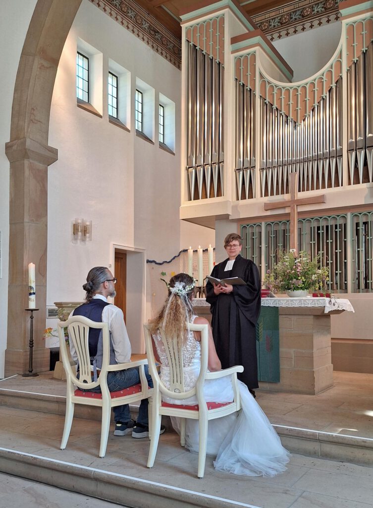Ein Ehepaar wird in einer Kirche von einer Gemeindepädagogin im Talar getraut.