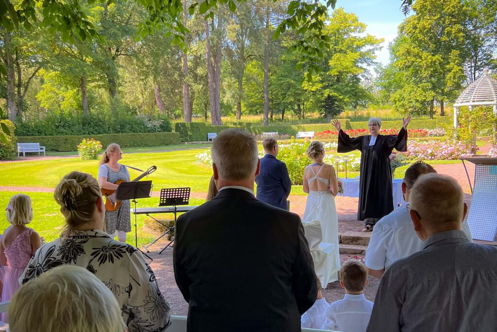 Eine Pfarrerin im Talar verheiratet kirchlich ein Ehepaar in einem Rosengarten in einem Park.