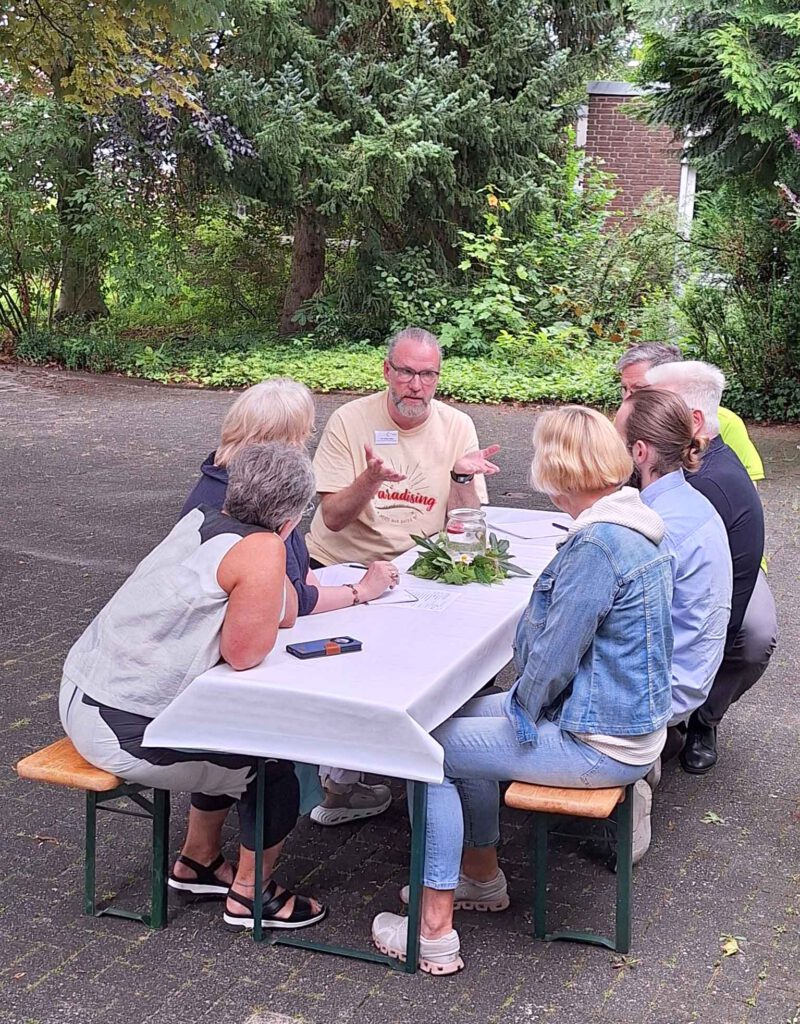 Eine Gruppe von Menschen sitzt draußen an einem Tisch und diskutiert.