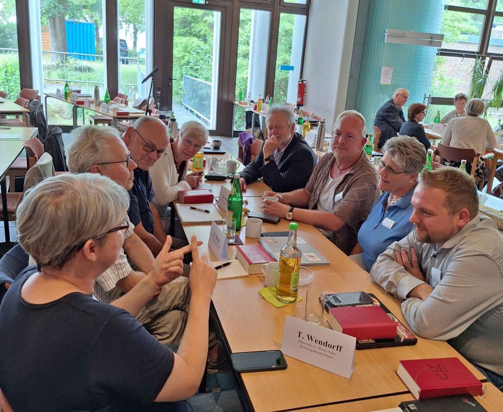 Ein Gruppe von Menschen sitzt im Tagungsraum an einem Tisch und diskutiert.