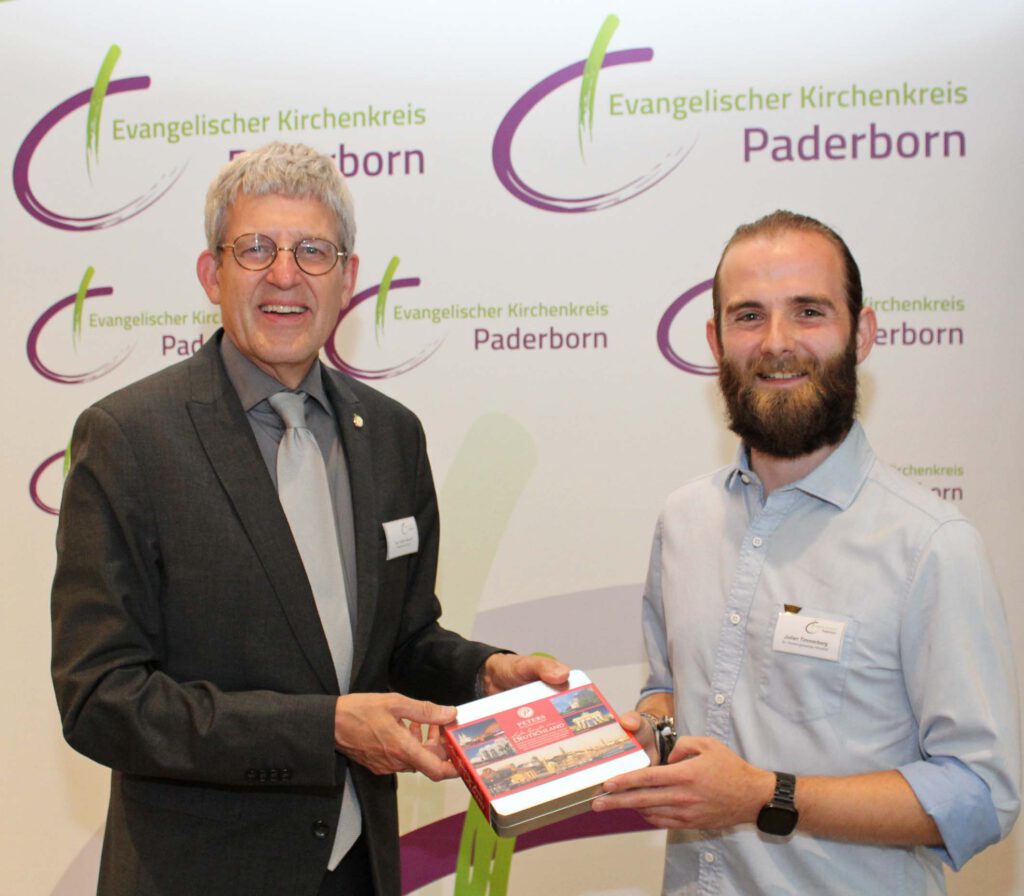 Eine neu gewählte Person erhält vom Vorsitzenden des Leitungsgremiums ein Präsent.