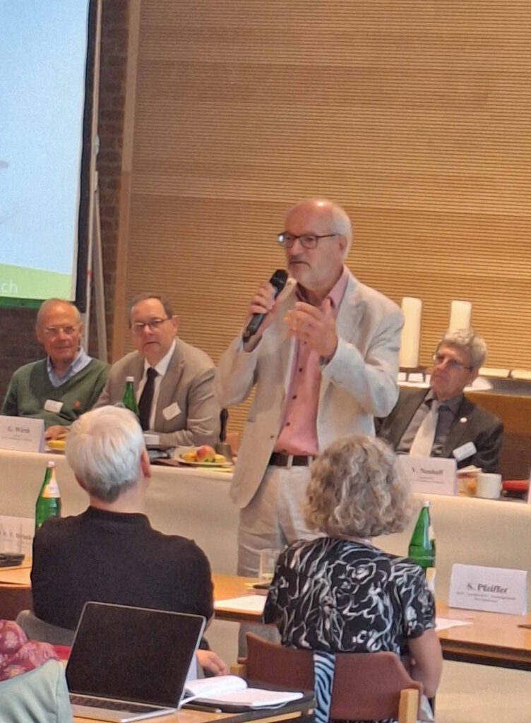 Ein Person mit einem Mikrofon in der Hand hält einen Vortrag.