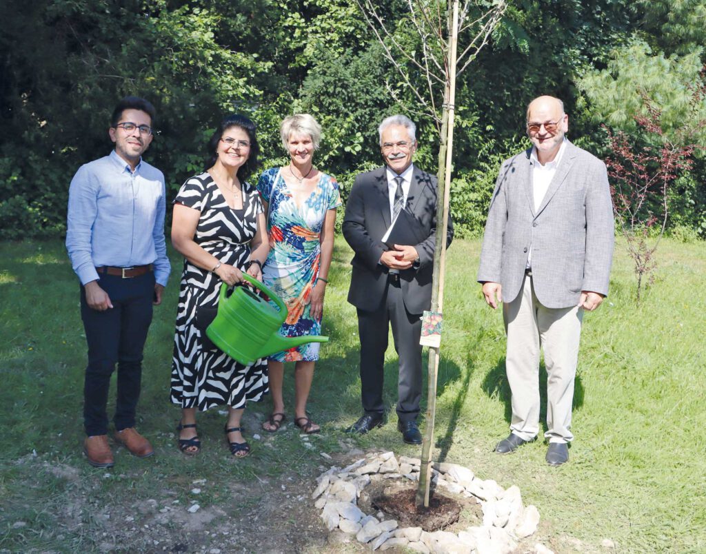 Menschen stehen hinter einem Apfelbaum, den sie gepflanzt haben.