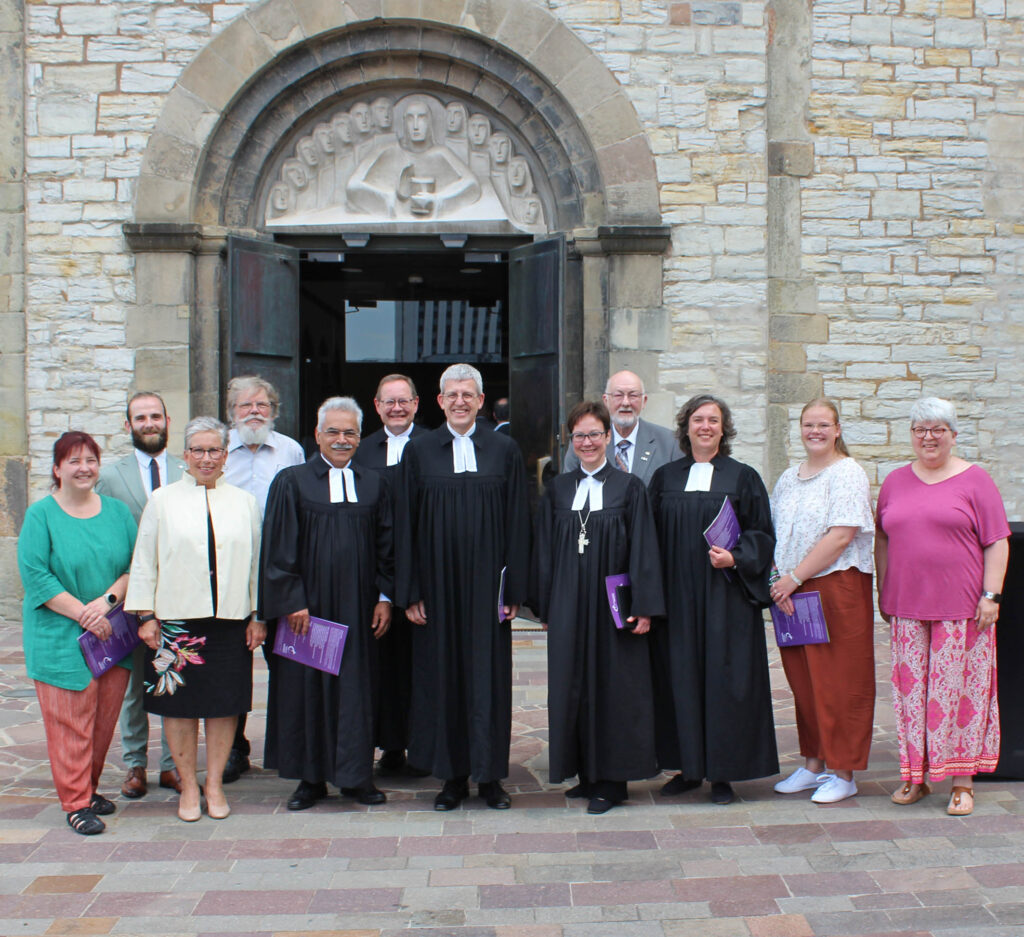 Eine Gruppe Menschen in ziviler Kleidung und im Talar stehen vor der Tür einer Kirche.