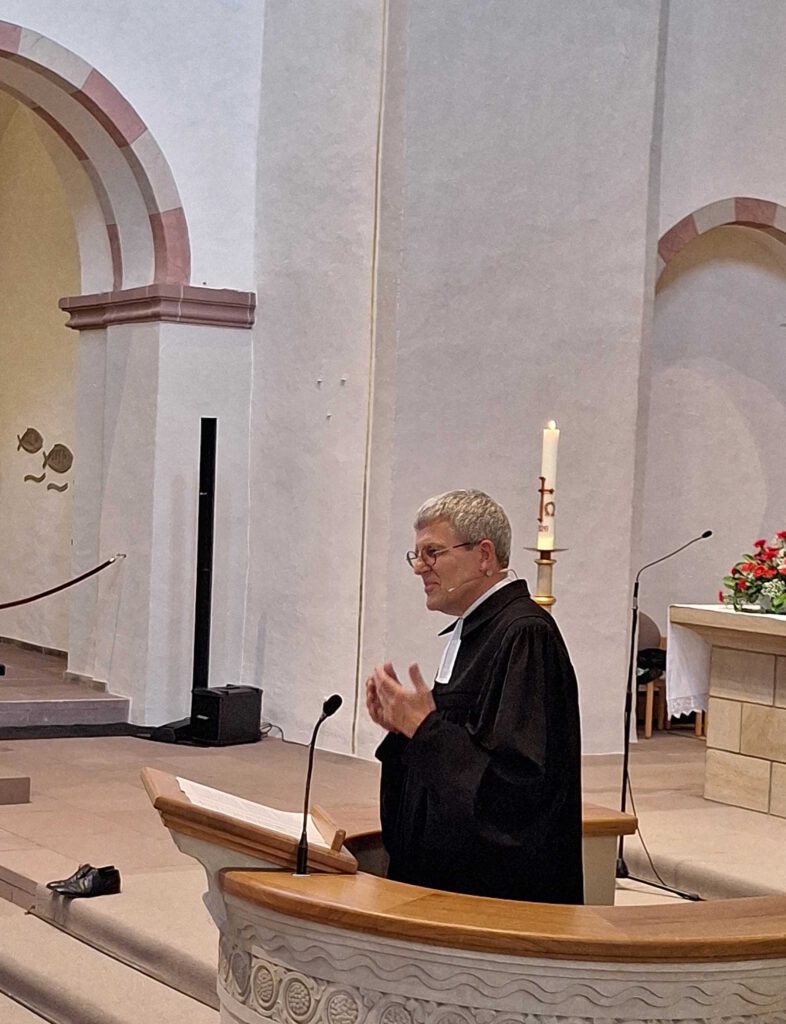 Ein Mann im Talar steht auf der Kanzel in einer Kirche und spricht.