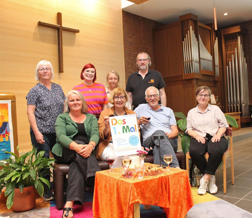 Menschen sitzen und stehen in einer Runde mit Sofas und Sesseln und einem Couchtisch in einer Kirche, eine Person hält ein Plakat in der Hand.