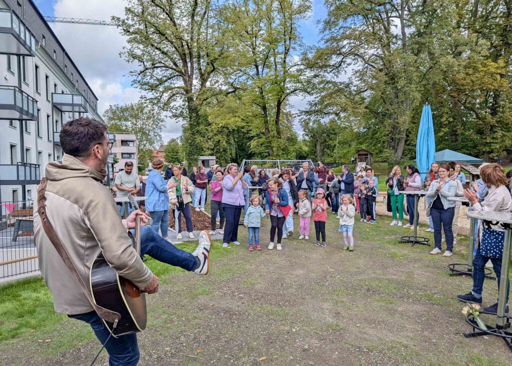 Ein Mann mit Gitarre spielt vor einer Gruppe Menschen Musik.