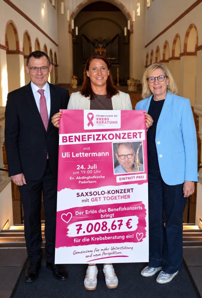 Drei Personen stehen in einer Kirche und halten ein Plakat mit einer Spendensumme in den Händen.