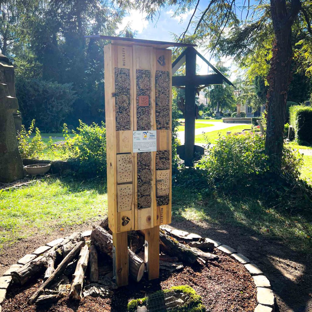 Ein Insektenhotel auf einer Wiese auf einem Friedhof.