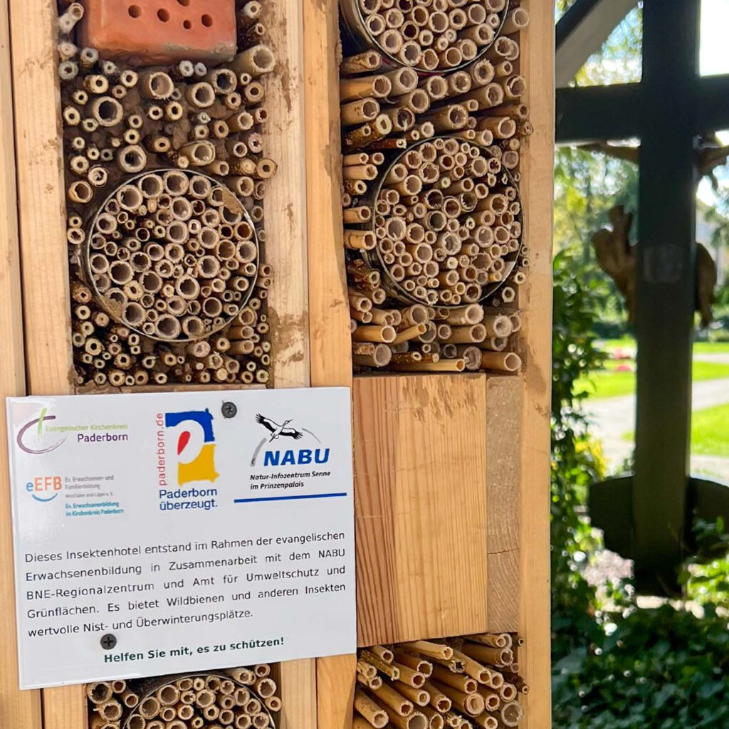 Ein Schild am Insektenhotel mit den Logos der beteiligten Institutionen und einem kurzen Text zur Erklärung.