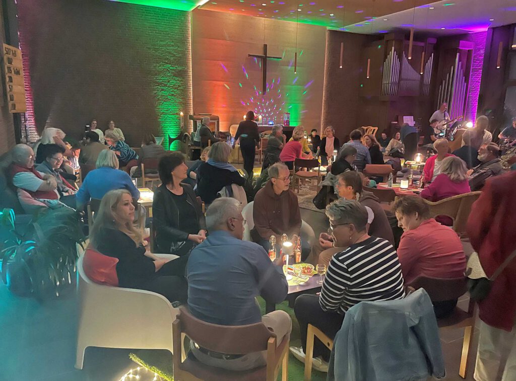 Menschen sitzen auf Sofas und Sesseln an kleinen Tischen bei einem Gottesdienst in einer Kirche.