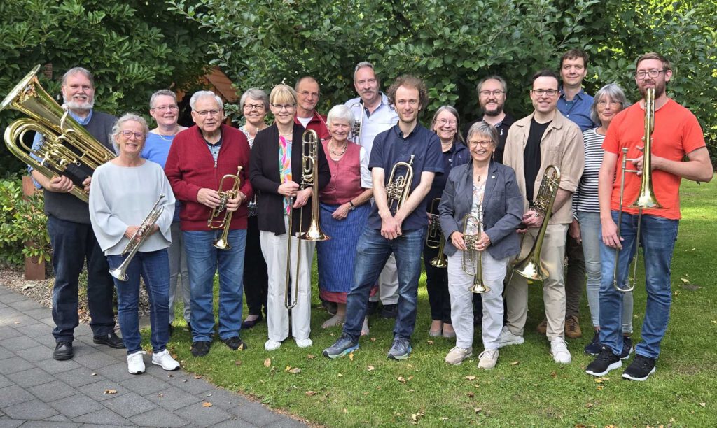 Eine Gruppe von Musikerinnen und Musikern mit ihren Blasinstrumenten stehen auf einer Wiese.