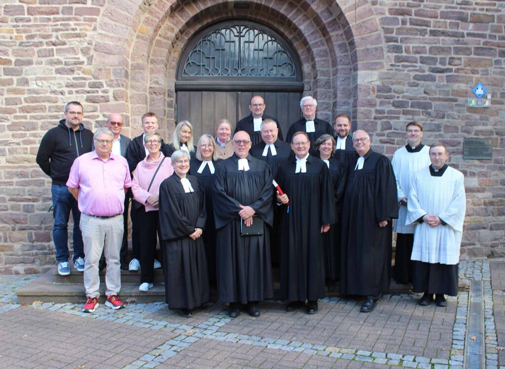 Vor der Tür einer Kirche haben sich Menschen, viele davon im Talar, aufgestellt.
