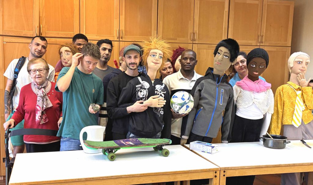 Menschen haben sich zusammen mit lebensgroßen Puppen hinter einem Tisch in einem Saal aufgestellt.