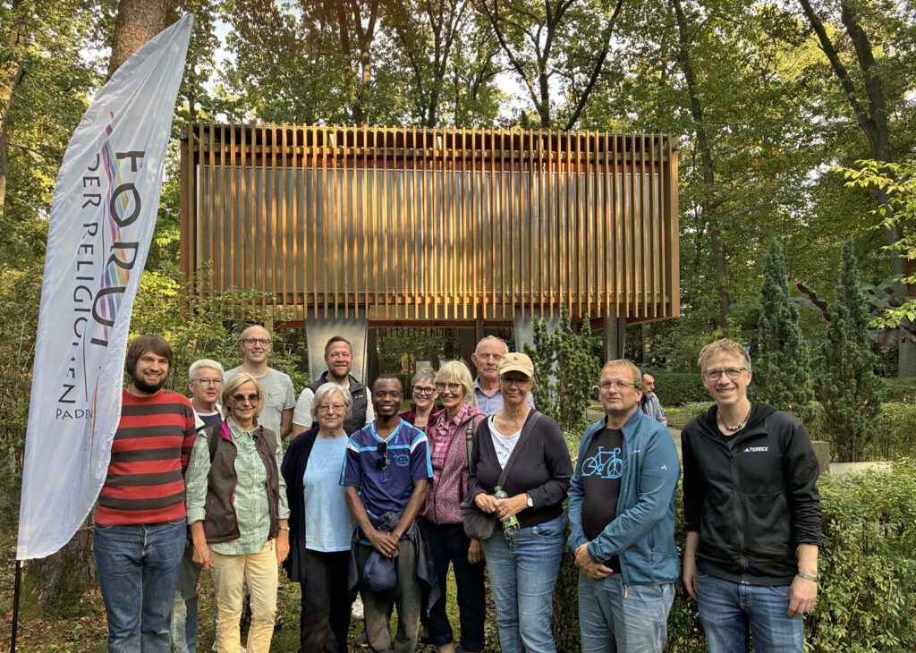 Menschen stehen im Grünen vor einem Pavillion.